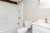 Modern bathroom with sleek white fixtures, a full bathtub, and stylish beige tiles.