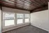 Inviting room with large windows providing ample natural light, featuring rustic wooden ceiling beams and fresh carpeting.