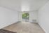 Bright and airy living room with plush carpet, large window doors opening to a scenic balcony, and fresh white walls.