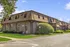 Charming brick apartment complex with unique roofline, featuring lush green landscaping and inviting atmosphere.