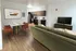 Modern apartment living space featuring an open kitchen with sleek appliances, a stylish dining area with a marble table, and a cozy green sofa facing a flat-screen TV.