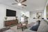 Chic open-plan living room with a modern, spacious feel; features stylish decor, a large wall-mounted TV, comfy seating, and a view into a sleek kitchen and elegant dining area.