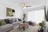 Inviting living room with a modern gray sectional sofa, vibrant accent pillows, and a sleek round wooden coffee table. Sunlight streams through vertical blinds, illuminating stylish decor and a lush indoor plant.