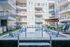 Contemporary apartment complex featuring a sparkling swimming pool, sun loungers, and private balconies, perfect for relaxation and leisure.