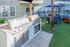 Modern outdoor grilling area with stainless steel barbecues and stylish patio seating under a vibrant blue umbrella, perfect for entertaining.