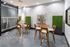 Modern communal space featuring elegant wooden chairs, stylish round tables, and vibrant greenery accents against a textured wall.