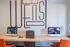 Modern workspace with sleek computers, a printer, and vibrant orange seating, accentuated by artistic wall decor.