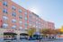 Modern urban apartment building with vibrant brick facade, tree-lined street, and inviting retail spaces below.