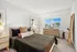 Bright and inviting bedroom with modern decor, featuring a cozy bed, stylish side tables, and a large window showcasing a beautiful outdoor view.