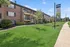 Charming brick apartment complex with well-maintained greenery and welcoming pathways under a bright blue sky.