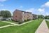 Charming brick apartment building with lush green lawn and tranquil suburban setting under a bright blue sky.