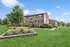 Charming brick apartment building surrounded by lush greenery and manicured landscaping on a sunny day.
