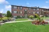 Inviting brick apartment building with lush landscaping and vibrant flower beds, showcasing a welcoming entrance under a clear blue sky.