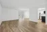 Bright and spacious open-concept living area with elegant wood flooring, flowing into a modern kitchen featuring sleek appliances and white cabinetry.