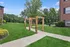 Charming outdoor area featuring lush green lawns, unique wooden archways, and a brick apartment exterior.