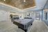 Luxurious recreational area featuring a sleek pool table and foosball table, surrounded by modern kitchen and dining area with stylish lighting and decor.