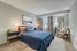 Inviting bedroom with modern decor, featuring a cozy bed with plush pillows, stylish nightstands, and elegant lighting, complemented by a large window with curtains and a comfortable reading chair.