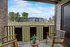Charming apartment balcony with cozy wooden seating, vibrant plant, and serene view of lush greenery and modern building.