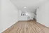 Bright open-concept living area with elegant wood flooring leading to a modern, fully equipped kitchen. Sleek white cabinetry and stainless steel appliances enhance the inviting and spacious ambiance.