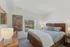 Charming bedroom with a plush bed, elegant artwork, and a scenic view through a large window.
