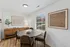 Inviting dining area with a round table, stylish wooden sideboard, and natural light streaming through wide windows, complemented by modern wall art.