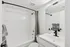 Modern bathroom showcasing a sleek white design, featuring a bathtub with a stylish curved shower rail, and elegant black fixtures.