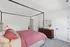 Elegant bedroom featuring a cozy four-poster bed with pink bedding, a wooden dresser with a stylish mirror, and soft carpeted flooring.