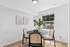 Bright and modern dining area with a round table, chic chairs, and elegant artwork, filled with natural light coming through a large window.
