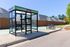 Modern bus stop with glass shelter and bicycle rack, set against a sunny suburban backdrop.