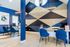 Modern office space featuring stylish blue chairs, sleek white desks, and geometric wall art, creating a vibrant and professional atmosphere.
