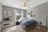 Cozy bedroom with modern decor, featuring a workspace with a desk, a comfortable bed with blue bedding, and ample natural light from a large window.