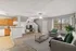 Bright and inviting open-concept living room with plush carpeting, modern furnishings, and an adjacent kitchen featuring wooden cabinetry. Large window with abundant natural light and cozy seating perfect for relaxation.