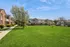 Charming apartment complex with landscaped green lawns, blossoming trees, and inviting brick facades under a bright blue sky.