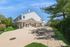 Charming two-story building with expansive outdoor patio, lush greenery, and inviting seating area under a clear blue sky.