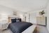 Bright and inviting bedroom featuring a cozy bed with navy and white pillows, stylish side tables with lamps, and chic decor elements.