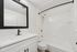 Sleek modern bathroom featuring a chic black-framed mirror, pristine white fixtures, and a luxurious bathtub.