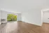 Bright living room with elegant hardwood floors and large windows opening to a lush green view.