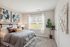 Elegant bedroom with a plush gray bed, abstract wall art, and ample natural light from a large window, complemented by green plant decor.