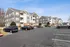 Charming three-story apartment complex with modern gray siding, spacious balconies, and ample parking space set against a clear blue sky.