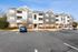 Modern apartment complex with attractive facade, ample parking, and landscaped surroundings under a clear blue sky.