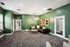 Modern lounge with vibrant green walls, featuring a cozy black leather sectional sofa and chic lighting, ideal for relaxation and socializing.
