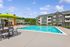 Inviting apartment complex with sparkling swimming pool, sun loungers, and vibrant green umbrellas set against a tranquil backdrop of modern architecture.