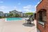 Inviting outdoor space featuring a sparkling swimming pool, elegant patio seating with bright green umbrellas, and a charming brick barbecue area, perfect for relaxation and social gatherings.