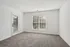 Bright, empty room with plush carpet and a large window, complemented by a glass door for ample natural light.