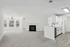 Bright open-concept living space featuring a modern kitchen with white cabinetry, spacious living room with elegant fireplace, and ample natural light from large windows.