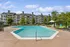 Inviting apartment complex with a sparkling outdoor pool, surrounded by lush greenery and modern lounge chairs.