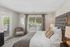 Elegant bedroom with luxurious tufted headboard, soft neutral tones, and ample natural light from large windows and glass door.