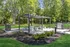 Charming outdoor space with modern pergola, picnic tables, and twin grills set amidst lush greenery, perfect for entertaining.
