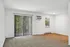 Bright living space with elegant carpeting, large sliding glass doors opening to a lush green view, and sleek air conditioning unit.