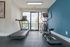 Bright and modern gym room featuring premium treadmill and elliptical machine with a view of the outdoor pool area, enhanced by sleek blue accent wall.